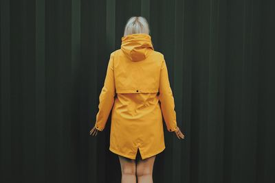 Rear view of woman standing against yellow wall