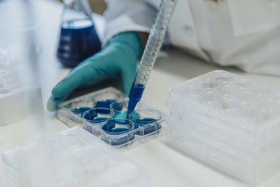 Laboratory assistant filling liquid in multi well plate at laboratory