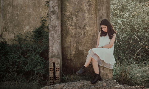 Young woman looking down while sitting by wall