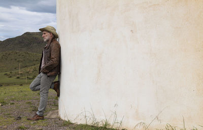 Adult man in cowboy hat standing against white wall in field