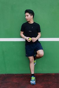 Young man holding tennis ball while standing against wall