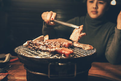 Woman preparing meat on barbecue at night