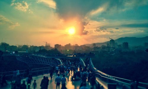 Crowd in city against sky during sunset