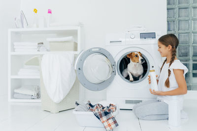 Smiling girl looking at dog in washing machine