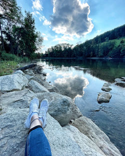 Low section of person by lake against sky