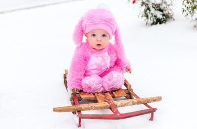 Portrait of cute baby girl sitting on sled during snow