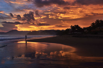 Mid distance view of man walking at beach against orange sky