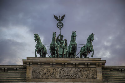 Low angle view of quadriga statue brandenburg gate against cloudy sky