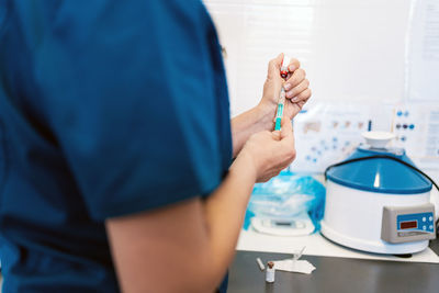 Unrecognizable doctor taking drug with syringe from vial while working in modern clinic