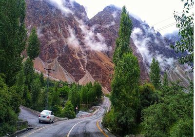 Road amidst trees and mountains against sky