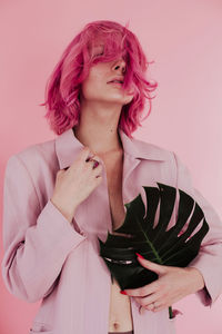 Young woman with dyed hair holding leaf while standing against colored background