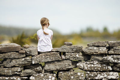 Girl sitting on stone wall, rear view