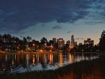 Illuminated buildings by lake against sky in city