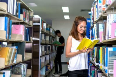 Students reading book while standing in library