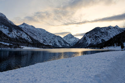 Scenic view of lake and snowcapped mountains against sky during sunset