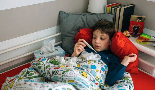 High angle view of boy holding thermometer on bed at home