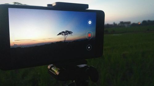 Close-up of camera on field against sky during sunset