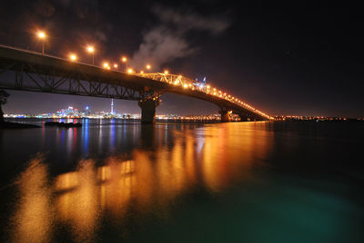 Illuminated bridge over river against sky at night