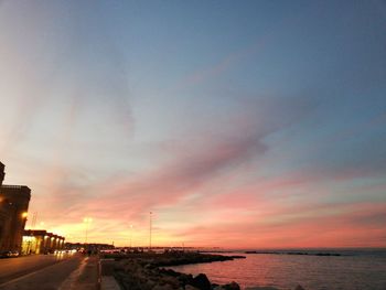 Road by sea against sky during sunset