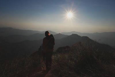 Rear view of woman standing on mountain against sky during sunset