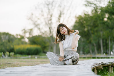 Young woman listening music while sitting on land against trees