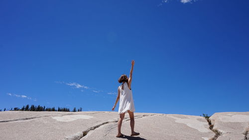 Rear view of woman with arms raised standing on cliff against blue sky