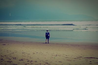 Rear view of man standing at beach against sky