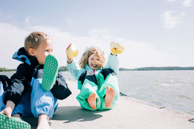 Siblings holding their shoes laughing at the beach on a windy day