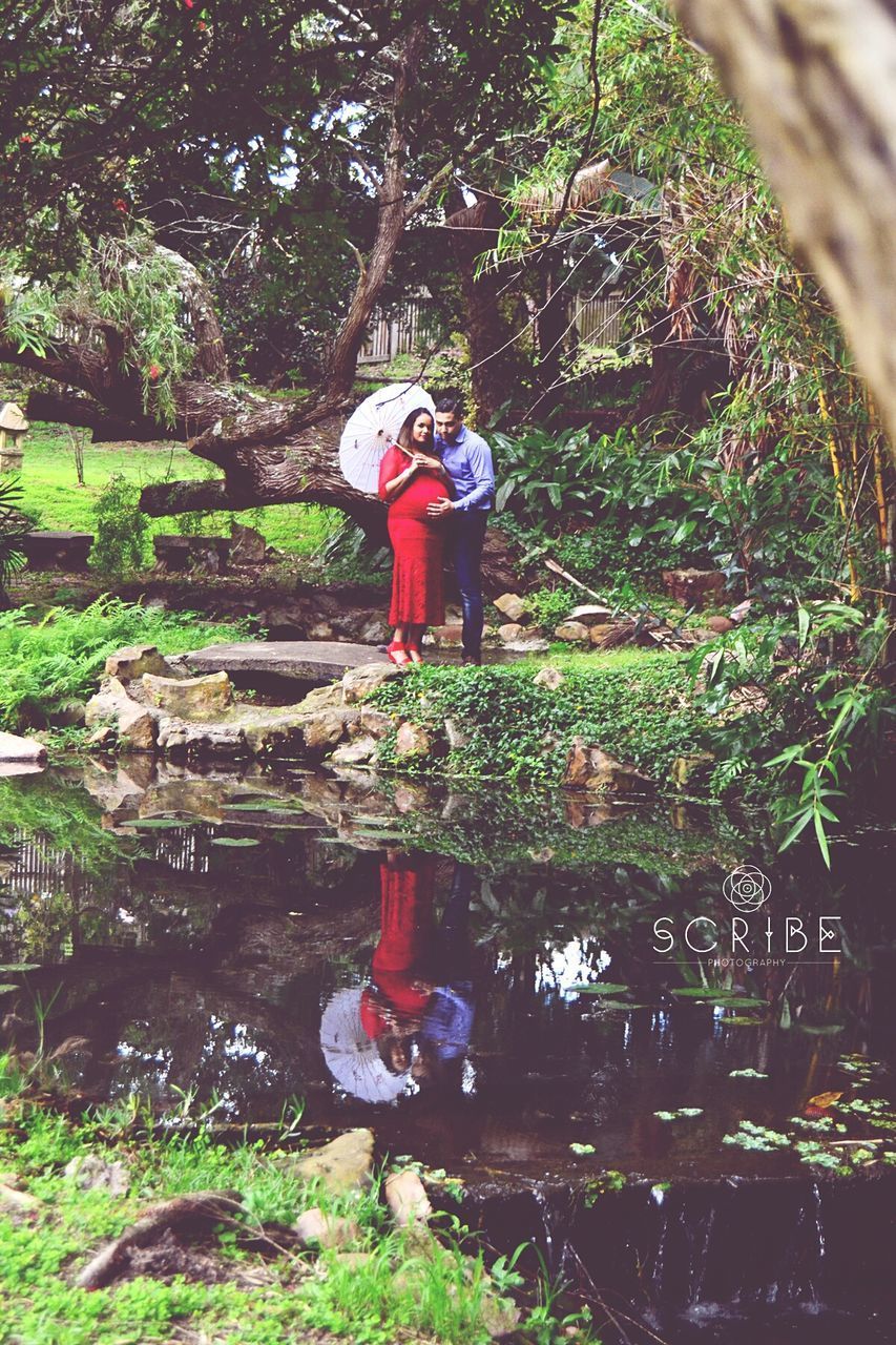 WOMAN PHOTOGRAPHING WHILE STANDING BY WATER IN FOREST