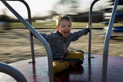 Portrait of cheerful boy sitting on merry-go-round