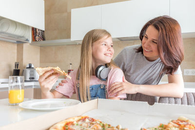 Mother looking at daughter eating pizza at home