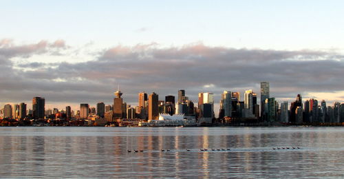 Sea by modern buildings in city against sky