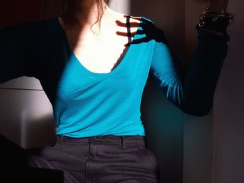 Midsection of woman sitting against wall at home