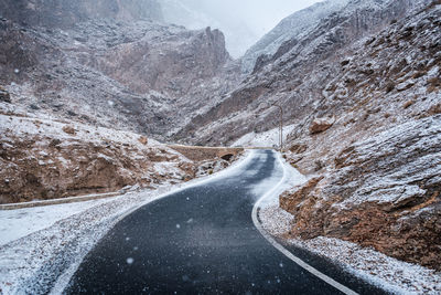 Snow covered road by mountain against sky