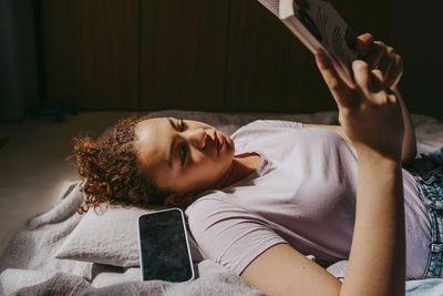 Teenage girl reading book while lying on bed