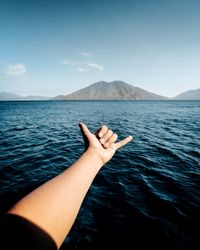 Cropped hand of woman gesturing over sea against sky