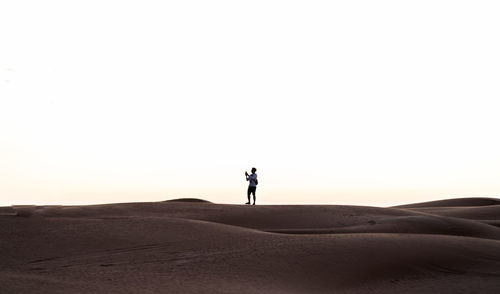 Man standing on sand dune in desert against clear sky