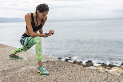 Concentrated fit female athlete in sportswear doing forward lunge exercise while warming up muscles during workout on promenade near sea