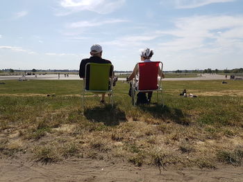 Rear view of men sitting on field against sky