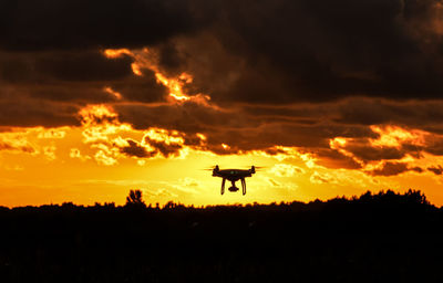 Silhouette airplane flying against dramatic sky during sunset