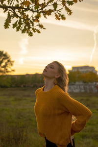 Woman looking away while standing on land against sky during sunset