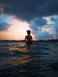 Silhouette man in sea against sky during sunset