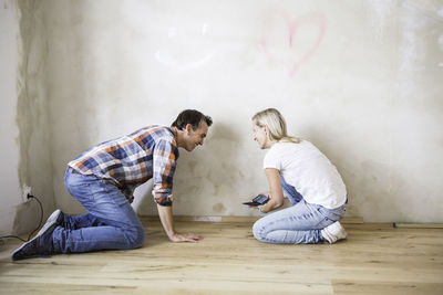 Side view of woman showing mobile phone to boyfriend kneeling on hardwood floor