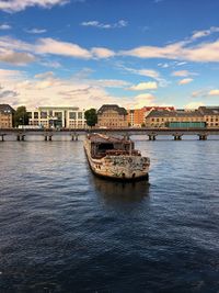 Boats in river by buildings in city against sky