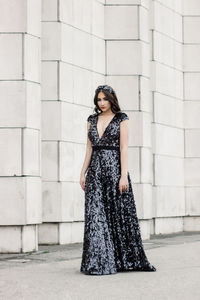 Portrait of beautiful woman wearing shiny evening gown while standing by wall