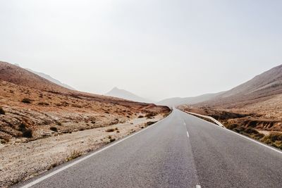 Empty road amidst mountains against clear sky