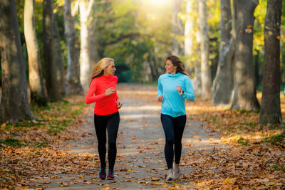 Woman exercising in public park with personal trainer in the fall.