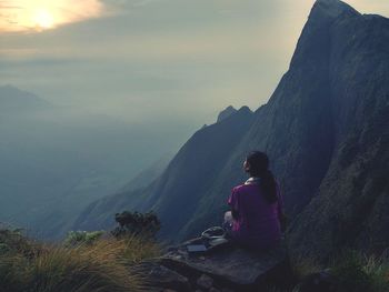 Rear view of man sitting on mountain against sky