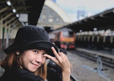 Portrait of smiling young woman gesturing while standing at railroad station platform