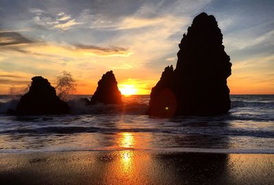 Low angle view of silhouette stack rocks in sea against sky during sunset